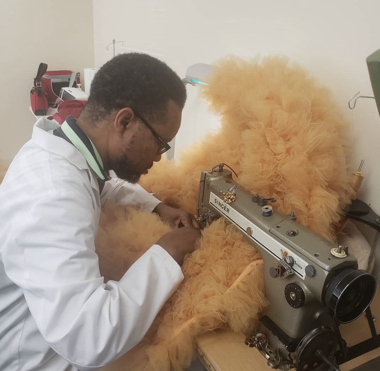 Craig Coates at his Singer industrial sewing machine, guiding a length of ruffled peach tulle